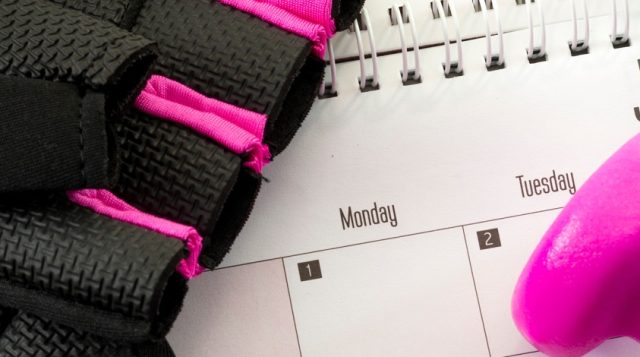 Calendar displaying the month of January, pink dumbbells, and a workout glove placed on a surface.