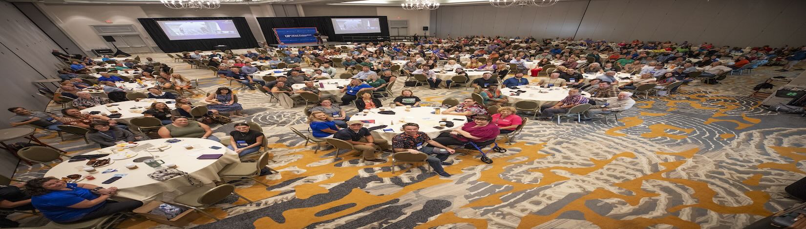 Photo of Extension Agents, administration, and guests sitting at conference tables smiling at camera.