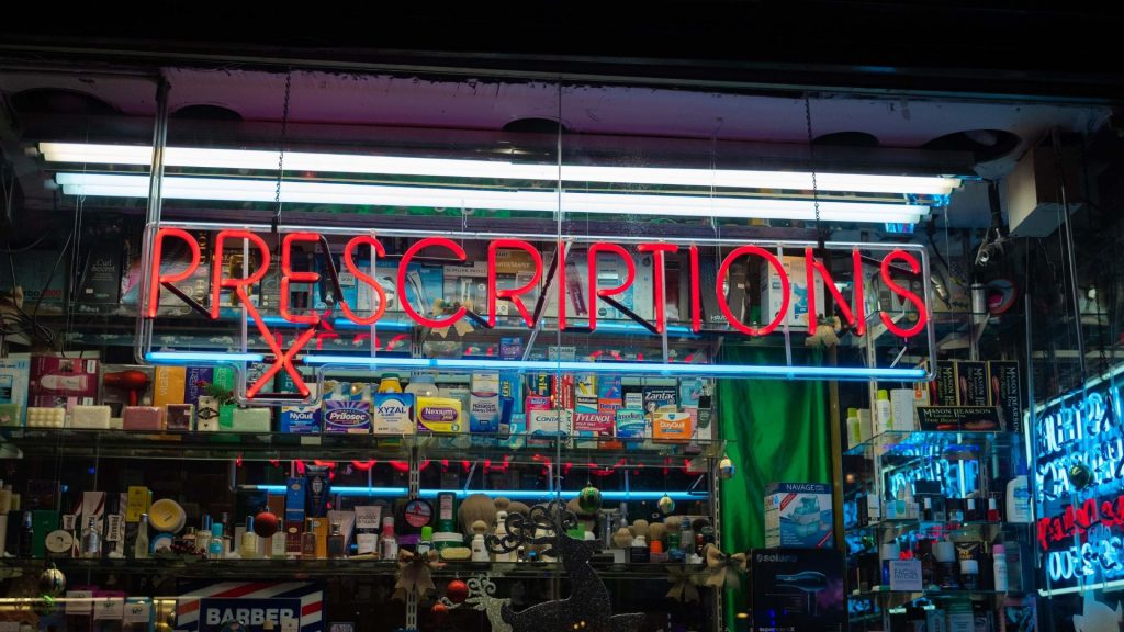 Image of drug store window with prescriptions neon sign