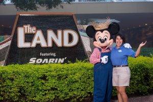 Clarissa and Mickey Mouse smiling in front of The Land sign
