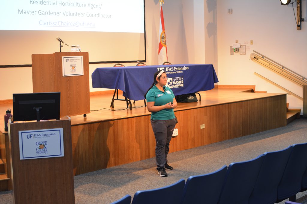 Clarissa standing in front of the stage in the auditorium ready to teach