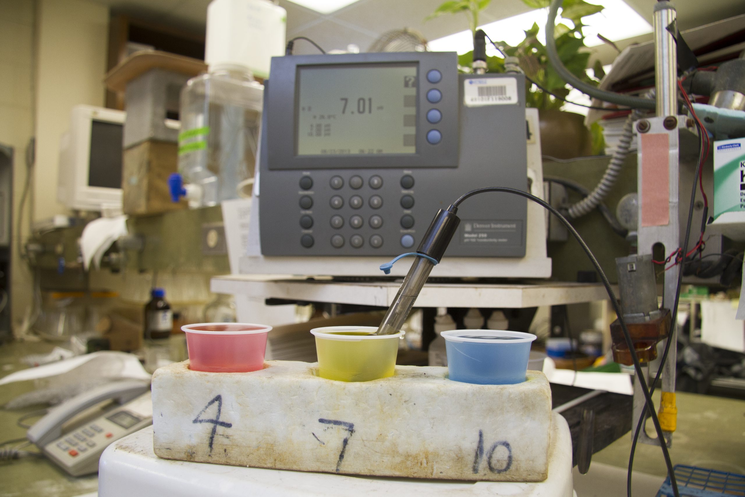 A PH testing machine at the UF Soils Testing Lab. There are 3 colored cups- pink is labeled 4, yellow is labeled 7, and blue is labeled 10. They are standards to known pH ranges to calibrate the machine for accuracy.