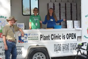 3 volunteers standing in the mobile plant clinic trailer ready to answer guest questions 