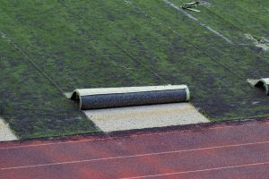 Old football field with used worn out artificial lawn turf rolls partly removed with copy space