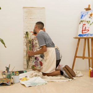 Man sitting on floor painting a picture.