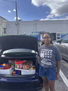 young girl in blue shorts and a gray tshirt in front of a car trunk open and full of peanut butter
