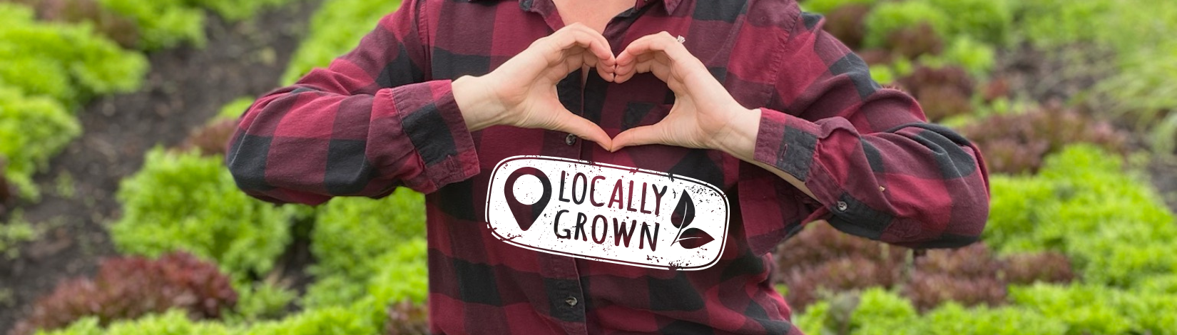 Hannah wearing a red and black flannel shirt with her hands in the shape of a heart in a field of lettuce
