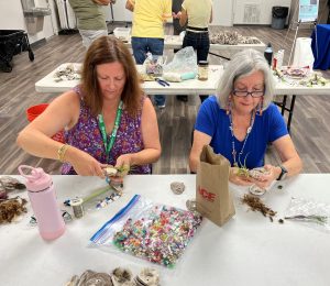 two women sitting at a table decorating their plant VOGs with beads and wires 