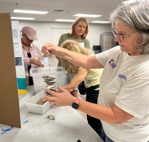 four people around a table. one is holing up a string of oyster shells 