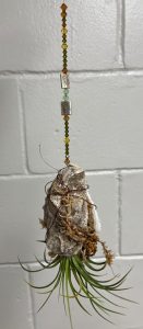 a pair of oyster shells with a plant between them hung from a wire with brown and green decorative beads