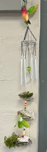 A plant VOGs with beads and plants between the shells hung from a windchime with a humming bird decoration 