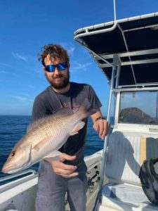 A mangrove snapper flying through the air after jumping out of a man's hands. The man is in the background on a boat. 