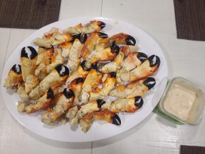 around 20 cracked stone crab claws on a white tray with a bowl of mustard sauce next to them 