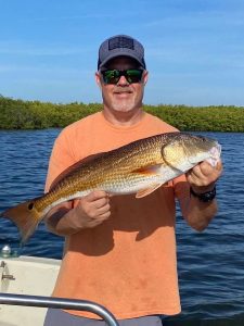 Man in hat and glasses holing a redfish in a boat.