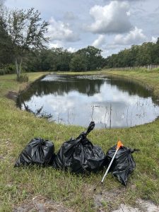 3 trash bags filled with garbage sitting in front of a clean pond 