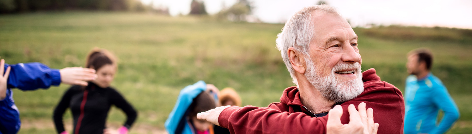 Large group of fit and active people doing exercise in nature, stretching.