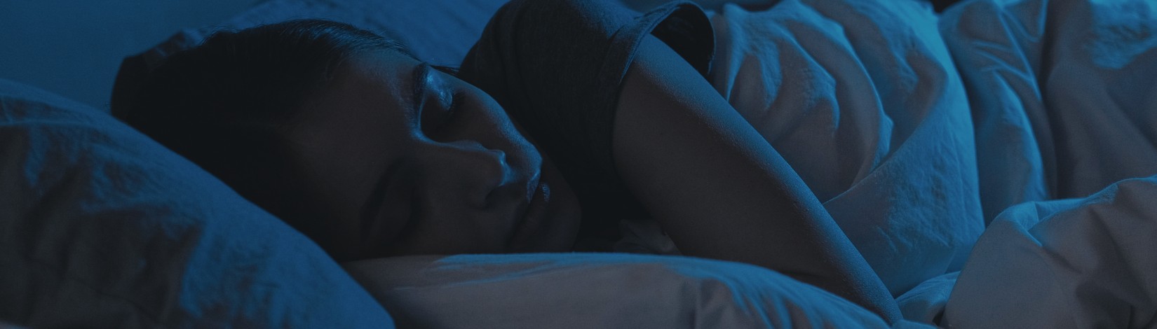 Night sleep. Relaxed woman. Bedtime rest. Tired lady with closed eyes lying in bed in dark home interior.