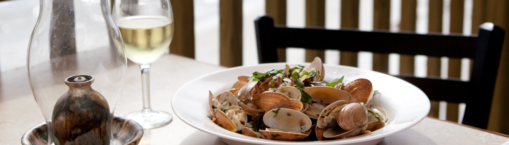 A plate of Sunray Venus clams set at an outdoor table overlooking the ocean.