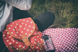 Girl sitting on a picnic cloth with a red back pack and a clear, reusable water bottle that says "My Bottle" on it. 