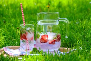 A glass pitcher with water infused with strawberries with a glass of ice water next to it. 