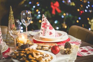 A setting at the dinner table for a holiday. There are wine glasses, cookies, and a napkin folded on top of a bowl and plate. The decor is holiday themed. 