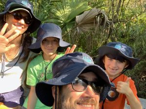Family of four, from left to right, mom, child, dad, child. All wearing their branded Adopt-A-Drain sunhats during an outing to maintain their adopted stormdrains.