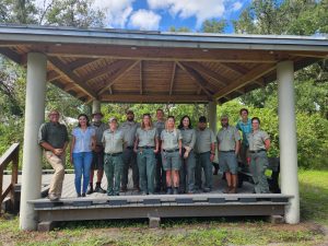 Group of county park rangers wearing their uniforms standing under a gazebo alongside course instructors