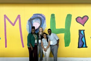 four people posing in front of a yellow mural