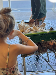 Young girl walking with parent, taking shopping cart full of peanut butter jars to car
