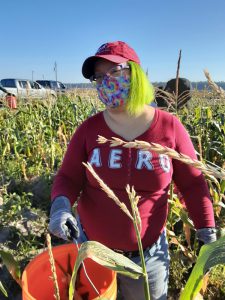 woman with mask on and holding a bucket in the corn field