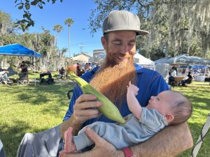 baby held by father with an ear of sweet corn in the position of a baby bottle