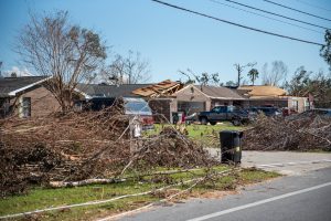 Storm-damaged homes with roof damage and fallen tree branches piled along the street.