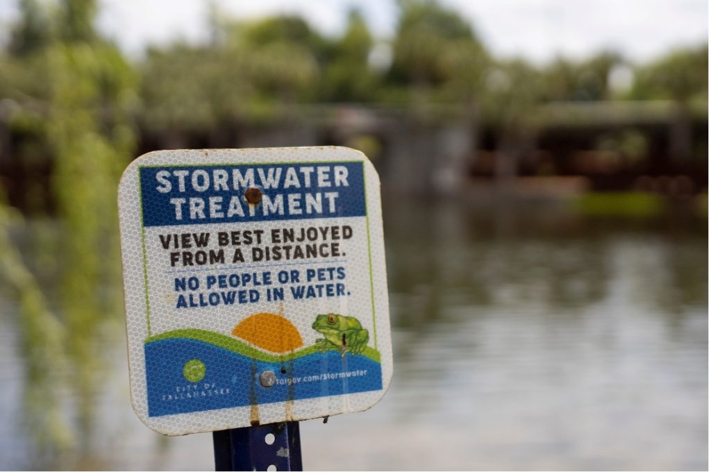 A metal sign reads "Storm Water Treatment: View best Enjoyed from a Distance. No People or pets allowed in water."