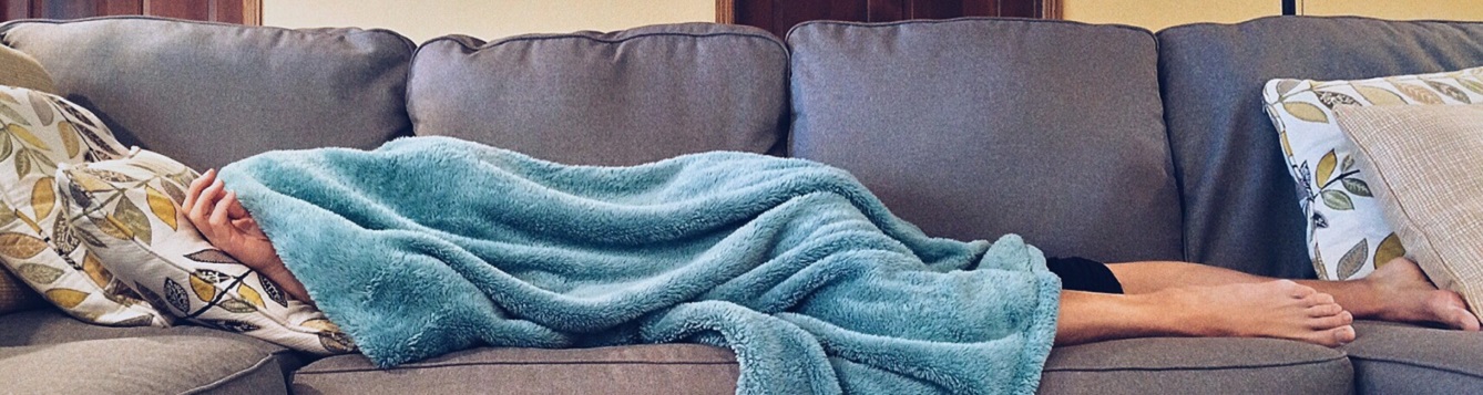 Person lying with head under blanket on couch