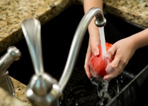 Washing a tomato under running water above a kitchen sink