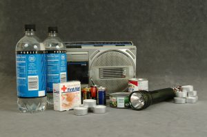 an assortment of disaster preparedness kit supplies, including water, bandages, batteries, flashlight and a weather radio