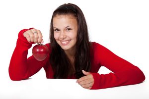 a smiling woman holds up a shiny-red apple by the stem. [credit: pixabay.com, public domain pictures]