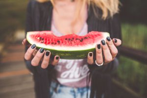 a person uses two hands (with black-painted fingernails) to hold up a watermelon wedge with several bites taken from it. [credit: pixabay.com, foundry co]