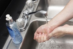 an individual washes their hands in a metal sink, with a container of hand soap nearby. [UF/IFAS Photo, Tyler Jones]
