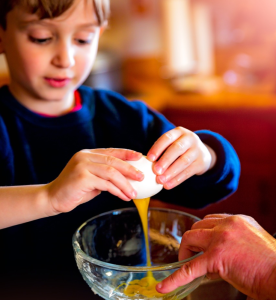 boy cracks an egg into a glass bowl held by an adult, while helping in the kitchen. [credit: pixabay.com, laterjay]