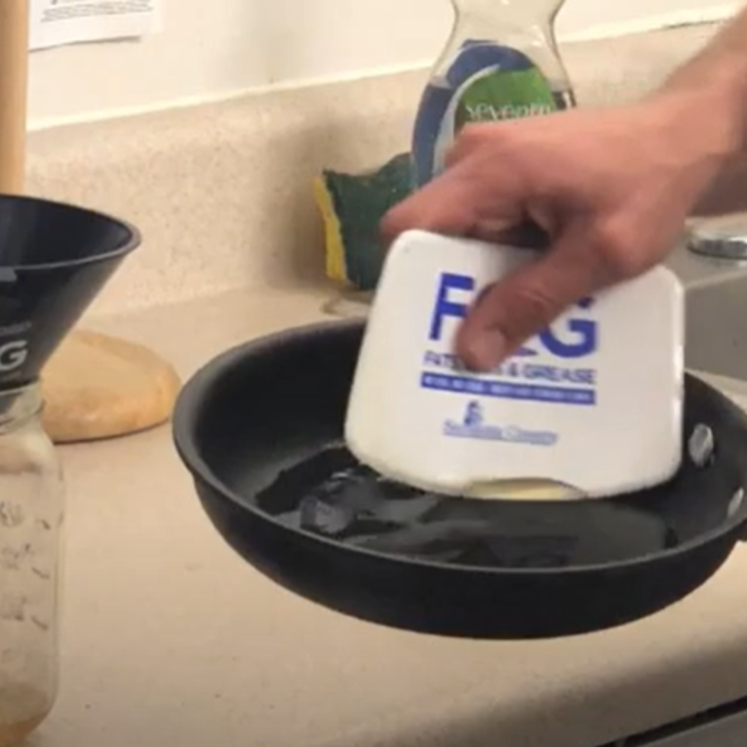 Grease being scraped out of a frying pan with a silicone spatula