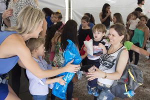 In a crowded tent full of people waiting in line, a woman and her son hand a care package to another woman and her son.