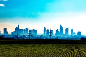 farmland and crops roll up to an urban skyline, with a bright-blue sky in the background. [credit: pixabay.com, Stilfee]