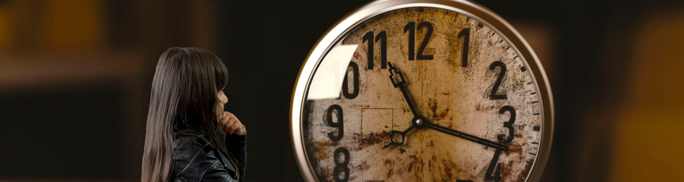 a girl wearing black clothes looks an an oversized analog alarm click. [credit: pixabay.com, un-perfekt]