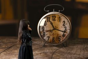 a girl in dark clothes stares at an oversized alarm clock, with her hand on her face. [credit: pixabay.com, un-perfekt]