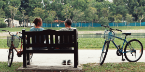 a man and woman take a break to sit on a bench near a lake in a grassy park, with their bicycles nearby. [credit: unsplash.com/ nguyen thu hoai]