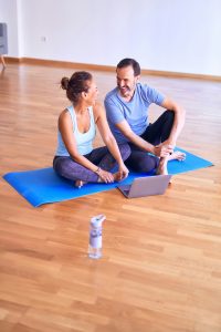 a man and woman share a laugh as they sit on a blue yoga mat. [credit: unsplash.com, kraken images]