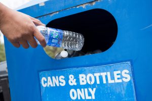 a hand with an empty plastic water bottle reaches into a blue bin to recycle the waste. [credit: uf/ifas, tyler jones]