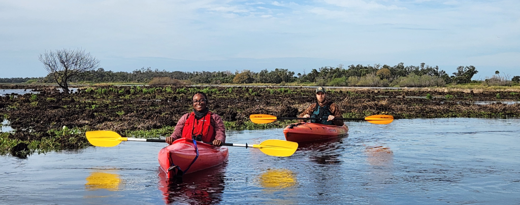 An image of a woman and man in separate kayaks, smiling at the camera.