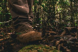 An image pg a person hiking through a forest with boots and long pants on.